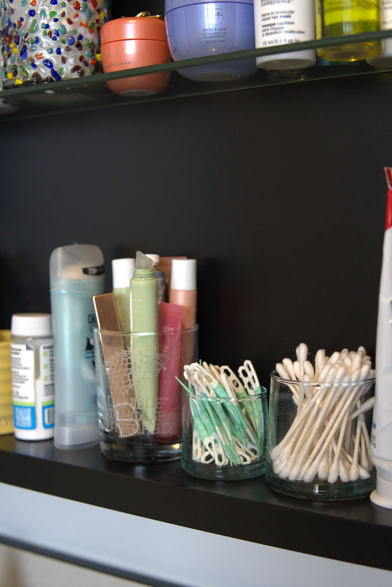 Shelves with personal care items including bottles, tubes, containers, cotton swabs, and a jar with cotton swabs on a black shelf.