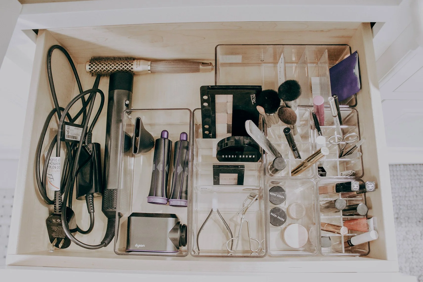 Organized drawer with hair styling tools, makeup products, and accessories, including curling irons, makeup brushes, scissors, and lip balm.