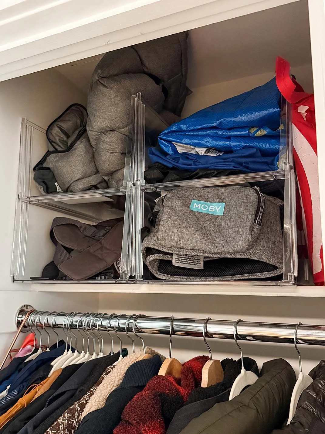 A closet with plastic storage bins filled with backpacks and outdoor gear, and a row of hanging clothes below.