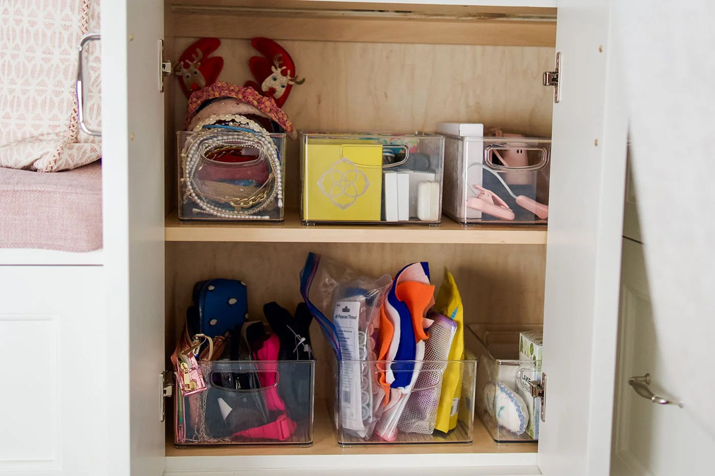 Inside a cabinet with various small transparent plastic containers holding jewelry, accessories, and craft supplies.