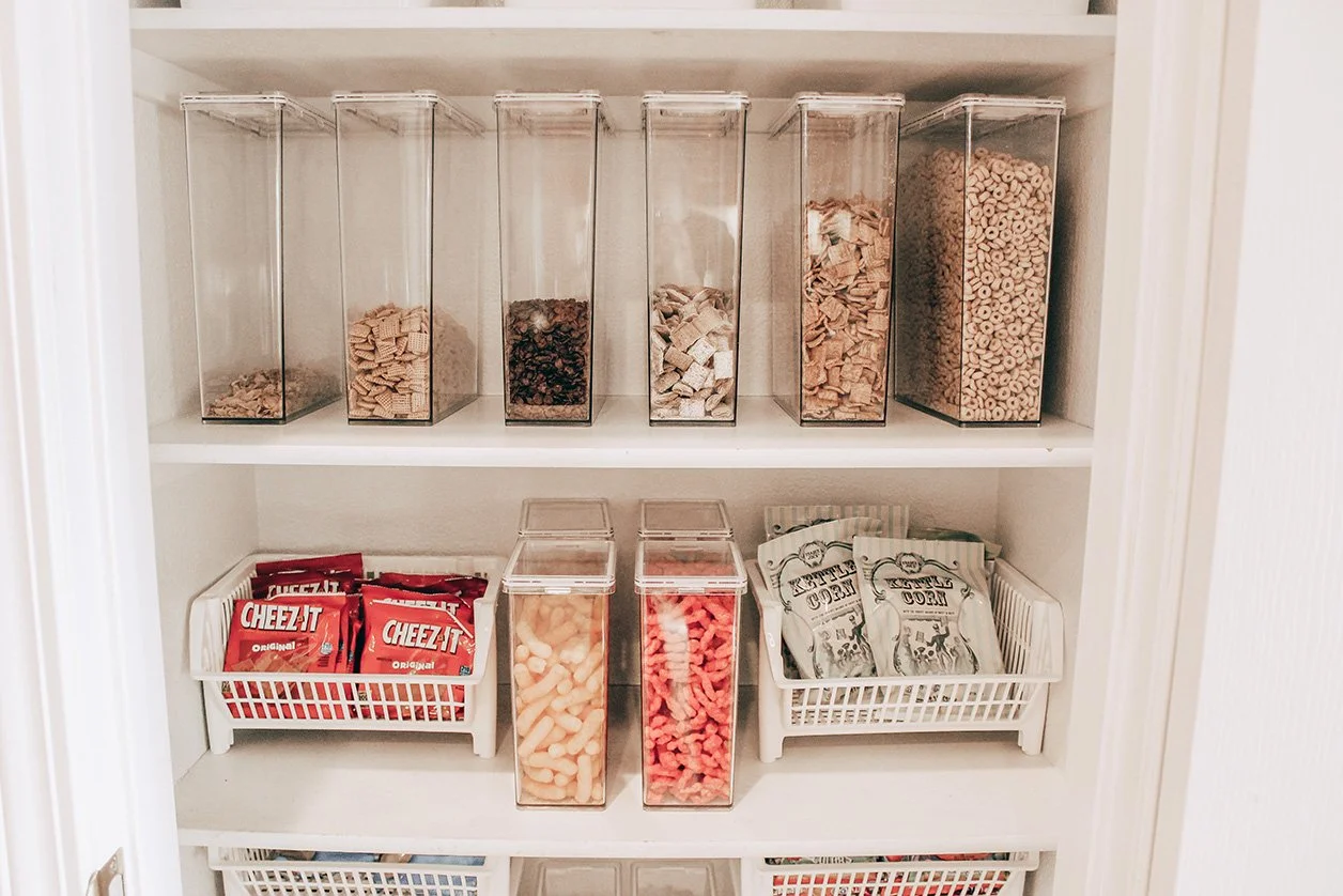 Pantry shelf with clear containers holding cereal, snacks, and pasta, with paper snack bags and Cheez-It boxes.