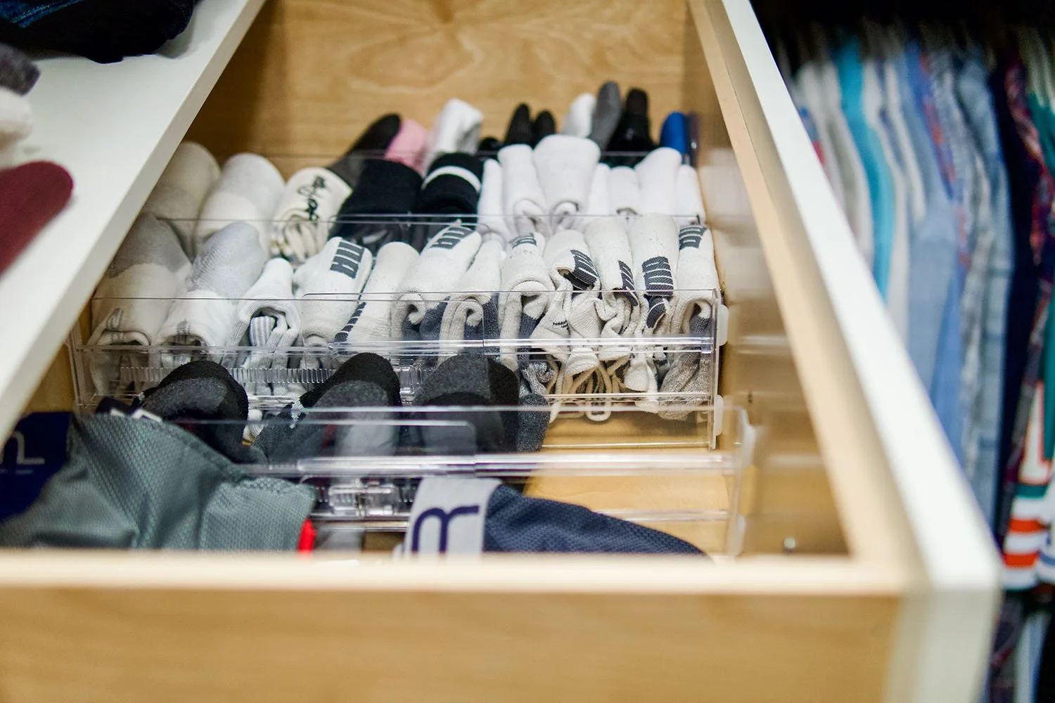 A drawer with organized white and black socks in a transparent pull-out tray in a closet.