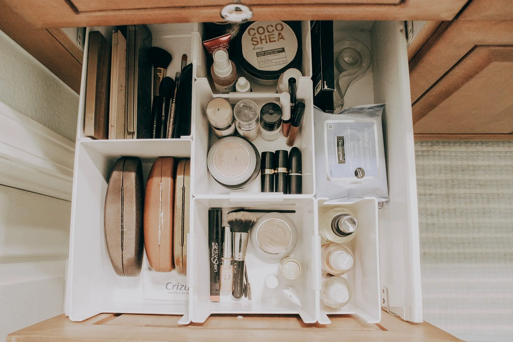 Organized drawer with various cosmetics and makeup products including brushes, lipsticks, moisturizers, and makeup remover wipes.
