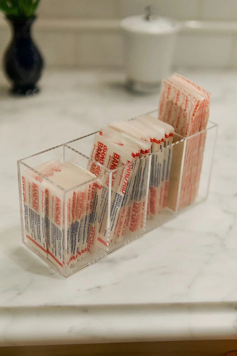 A clear plastic organizer with multiple compartments holding packets of sugar on a white marble countertop.