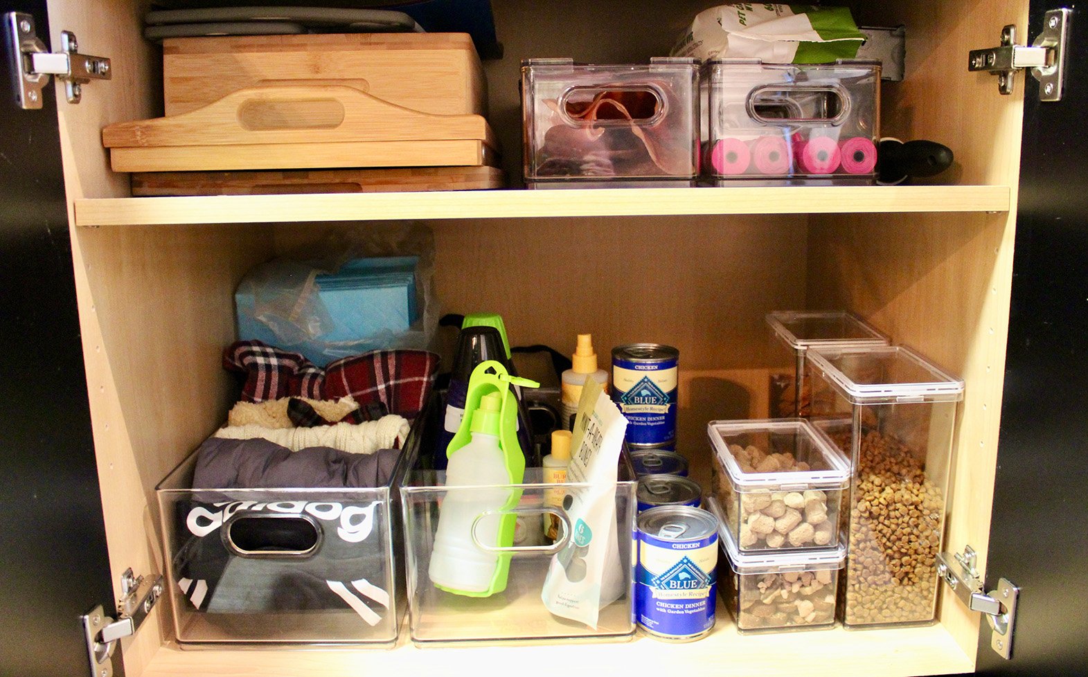 A wooden cabinet with pet supplies and food containers, including canned and dry pet food, cleaning sprays, and storage boxes for pet treats and accessories.