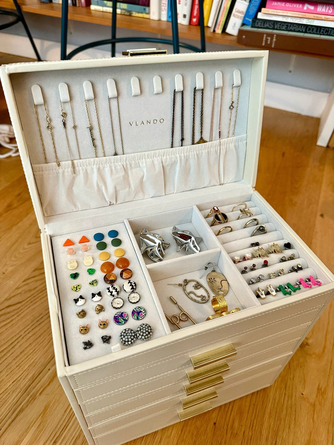 A jewelry box containing various earrings, rings, and necklaces, with a bookshelf in the background.