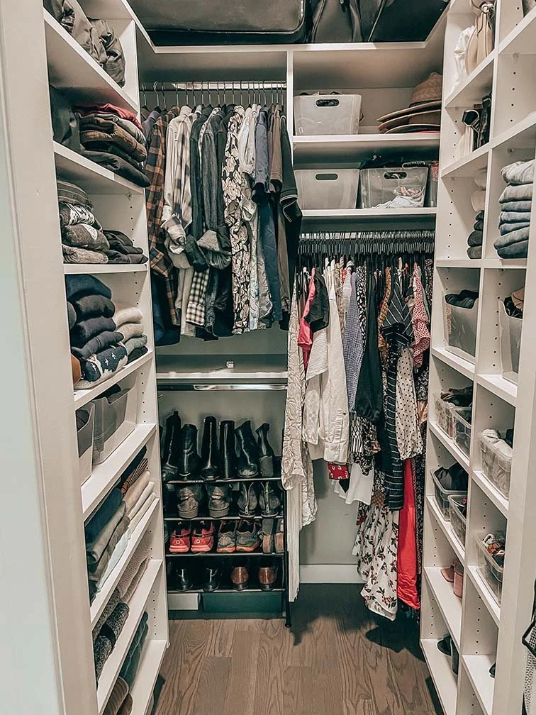 A walk-in closet with neatly organized shelves on both sides, clothing hanging in the center, and shoe racks at the bottom.