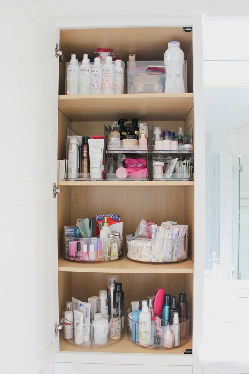 Open cabinet with skincare, makeup, and beauty products organized in clear containers on four shelves.