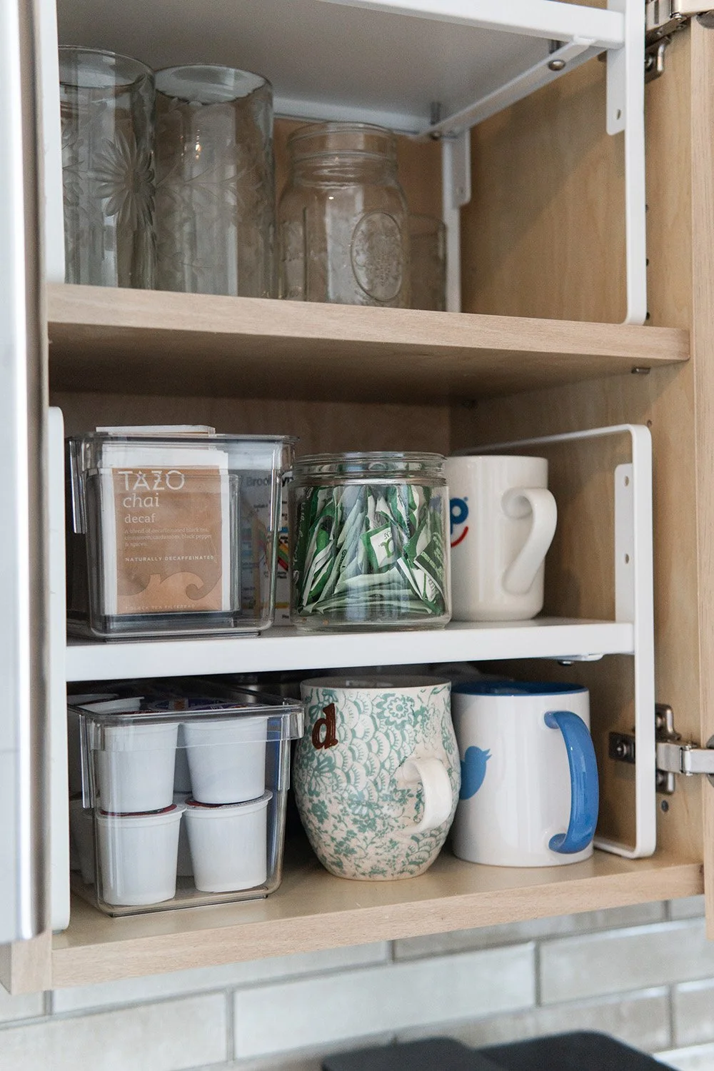 Open kitchen cabinet with glass jars, ceramic cups, and mugs with various designs.