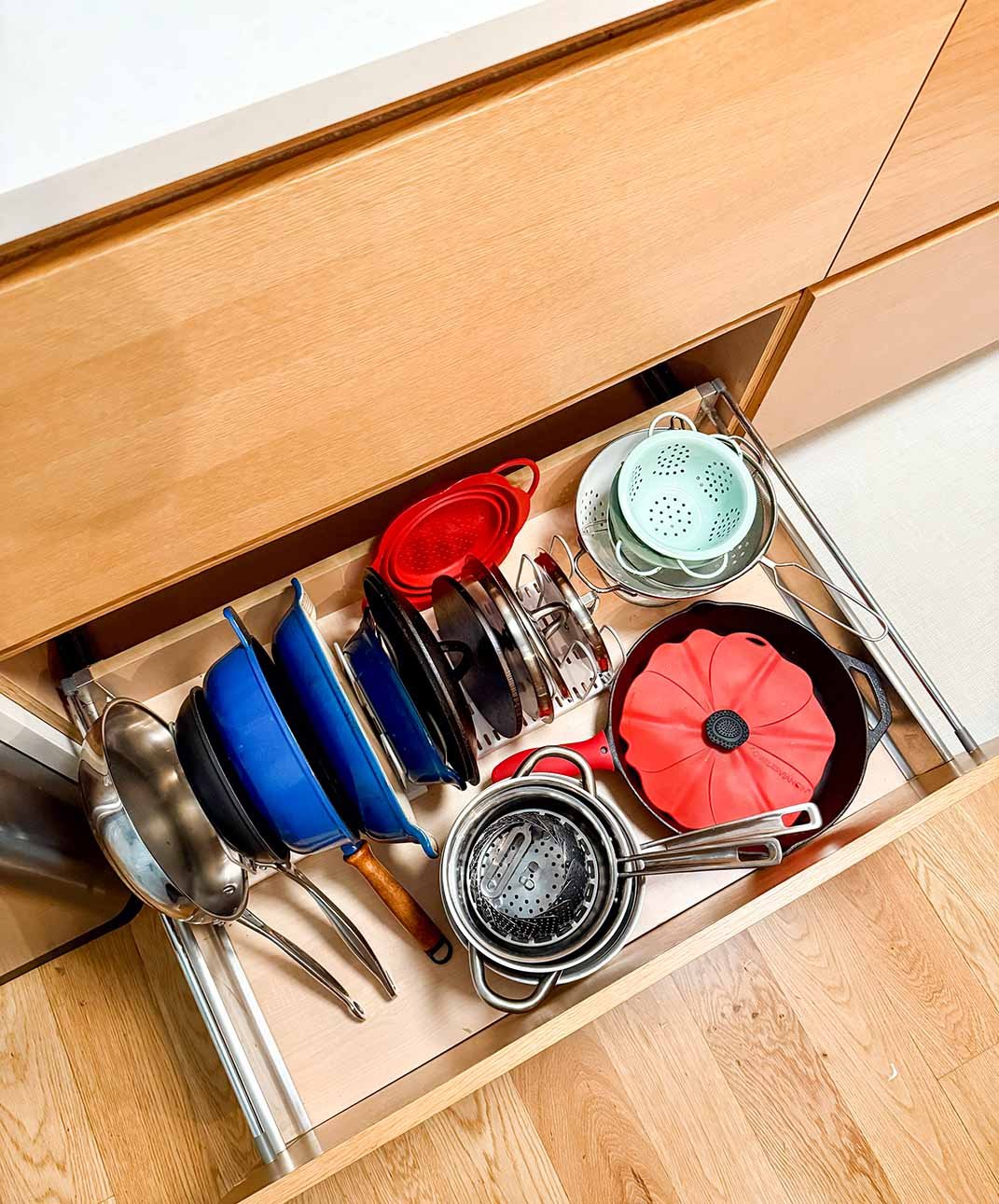 Open kitchen drawer with various cookware including pots, pans, strainers, and a silicone lid.