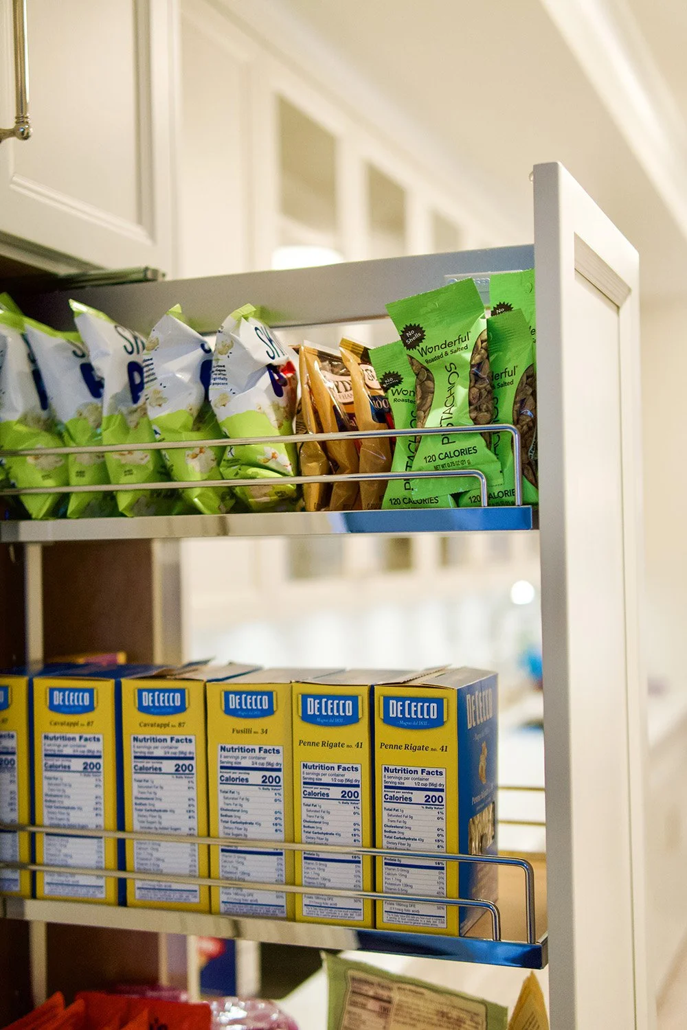 Shelf with snack bags and boxes of DeCecco pasta in a kitchen pantry.