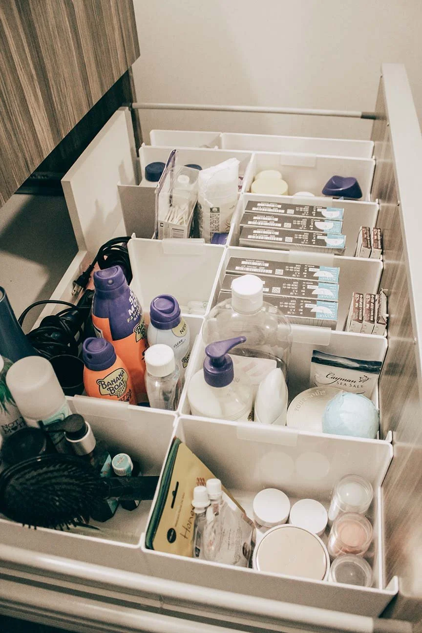 Open bathroom drawer filled with toiletries and personal care items including lotions, hairbrush, toothpaste, toothbrushes, and medications.
