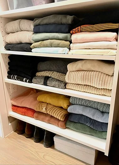 Stacked folded clothes on white shelves with shoes and storage box below.