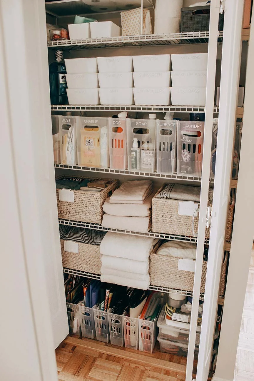 A closet with multiple shelves holding organized storage bins, towels, and various household items.