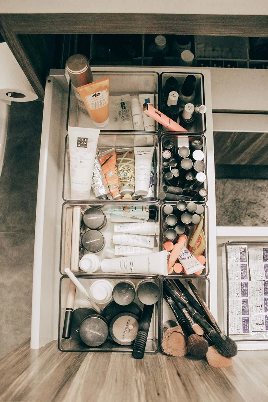Top view of a drawer organizing various beauty and skincare products, including makeup brushes, tubes, jars, and bottles.