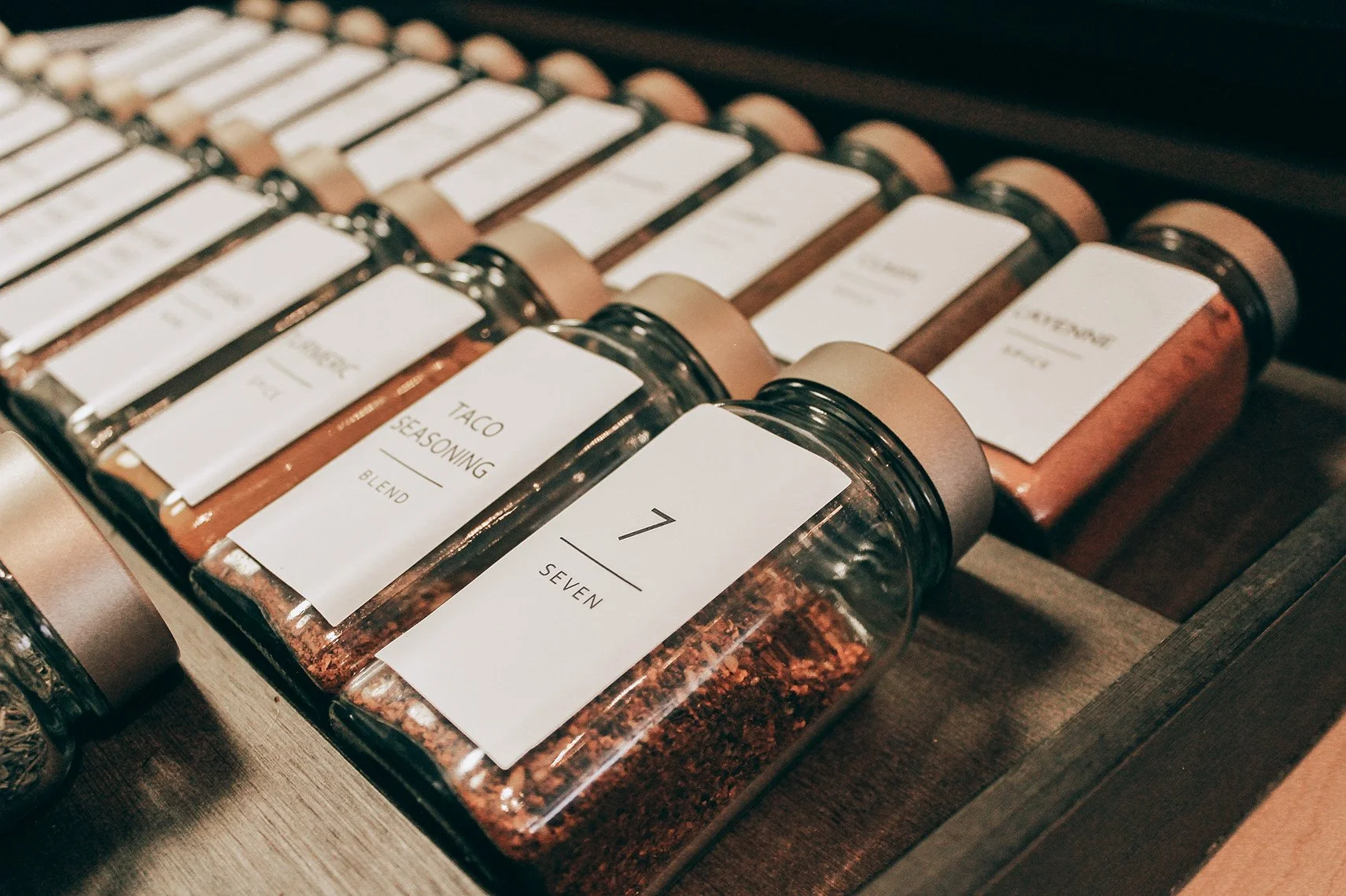 Collection of spice jars with white labels, including one labeled '7 Seven' and another labeled 'Taco Seasoning Blend'.
