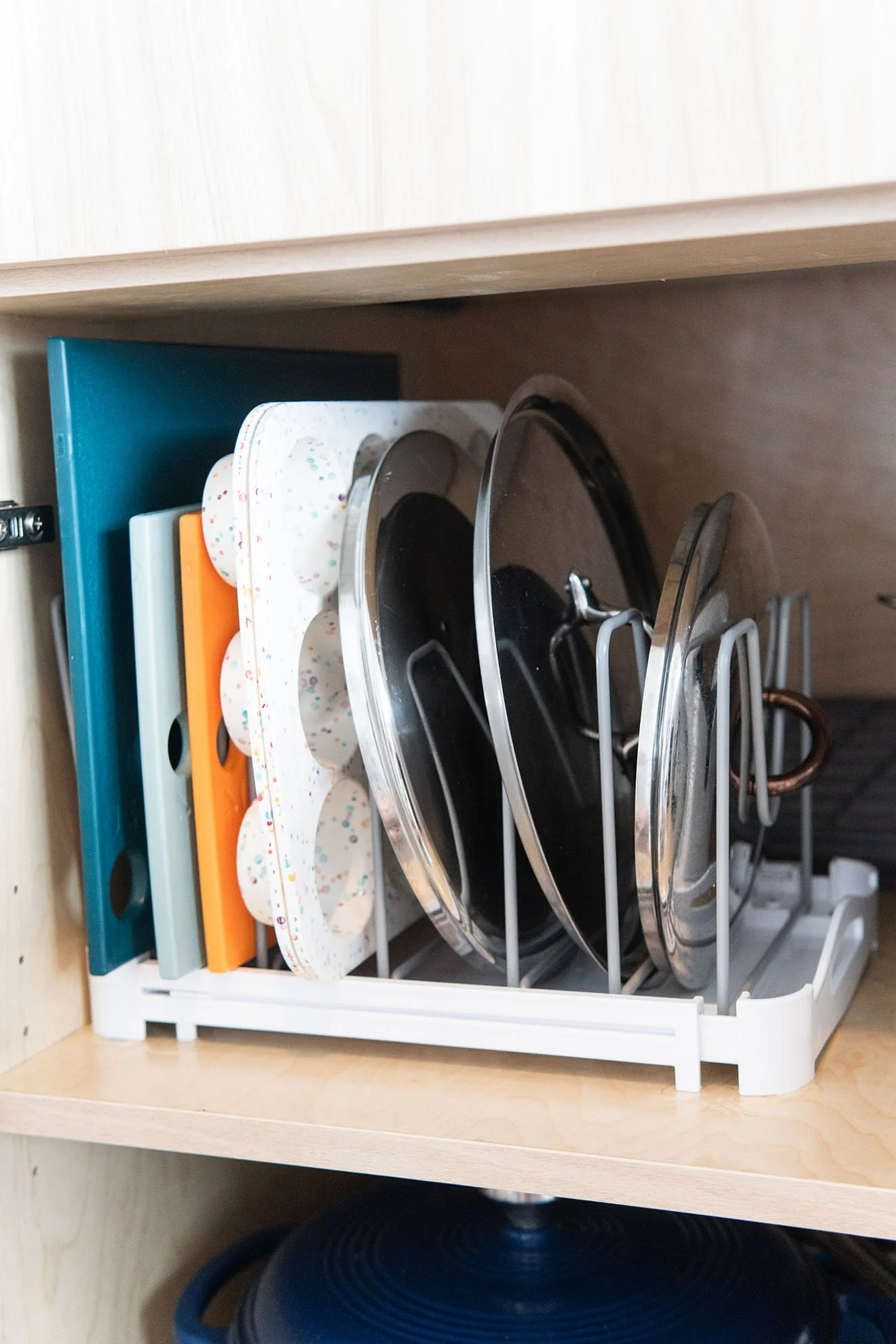 Kitchen cabinet with vertical organizer rack holding pots, pans, and cutting boards, with a wooden cabinet above.