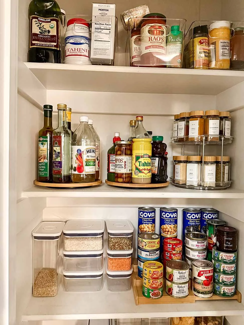 Pantry closet with bottled oils, vinegar, spices, canned goods, and dry grains in clear plastic containers.