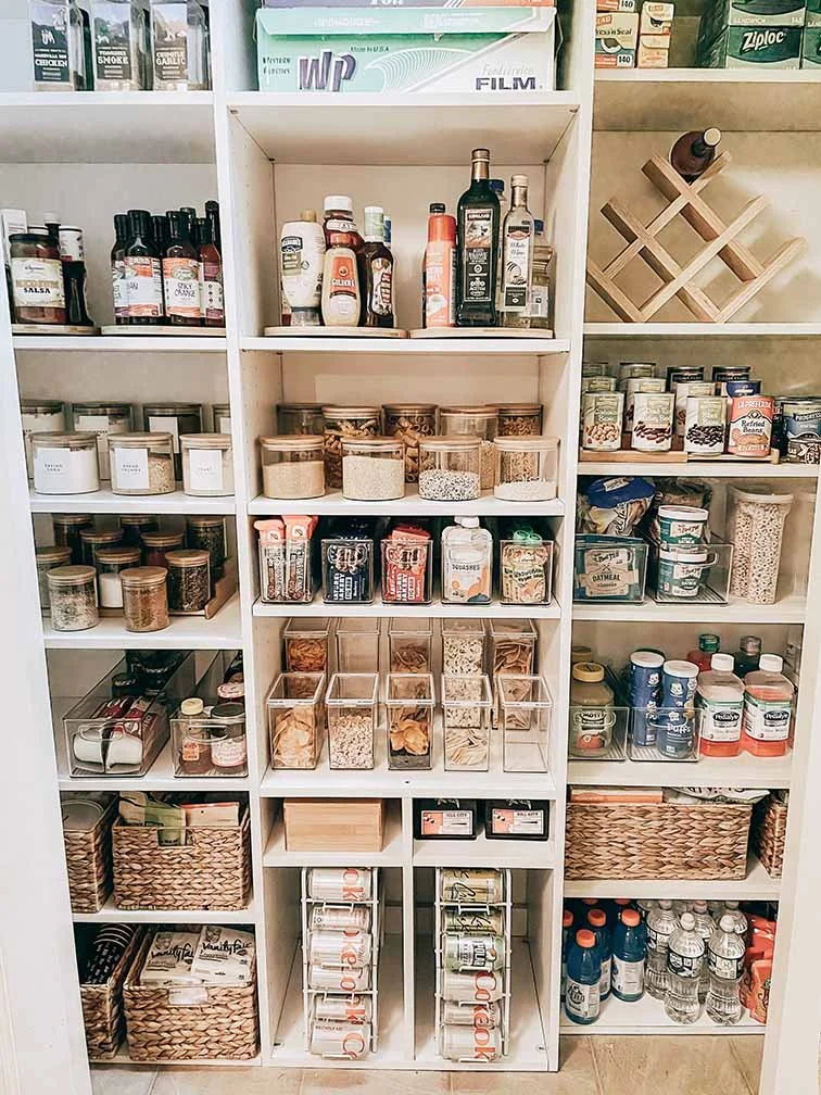 Organized pantry shelves with jars, bottles, and containers of spices, herbs, grains, and bottled drinks.