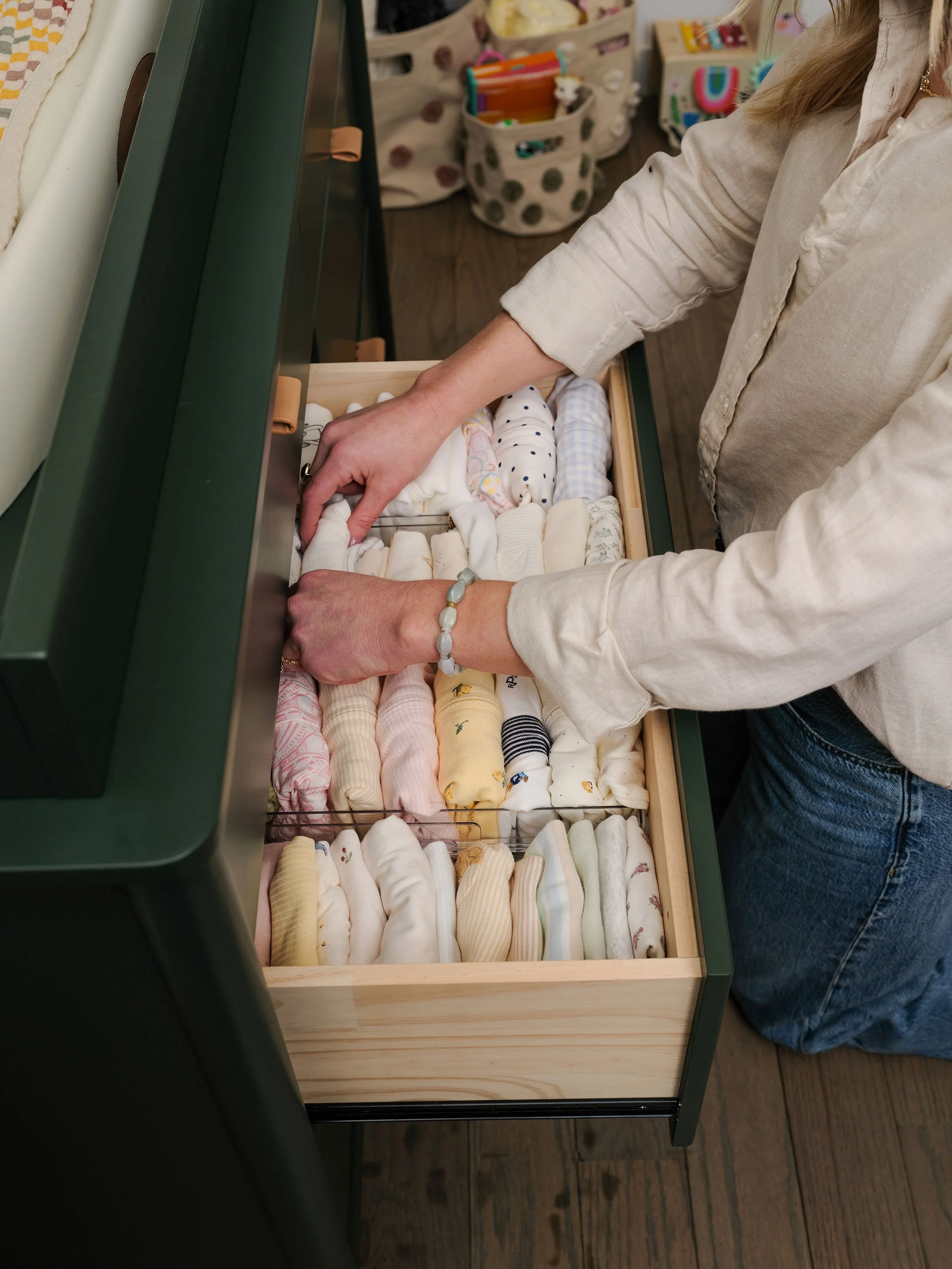 A person organizing a collection of folded baby clothes or fabric items inside a wooden drawer.