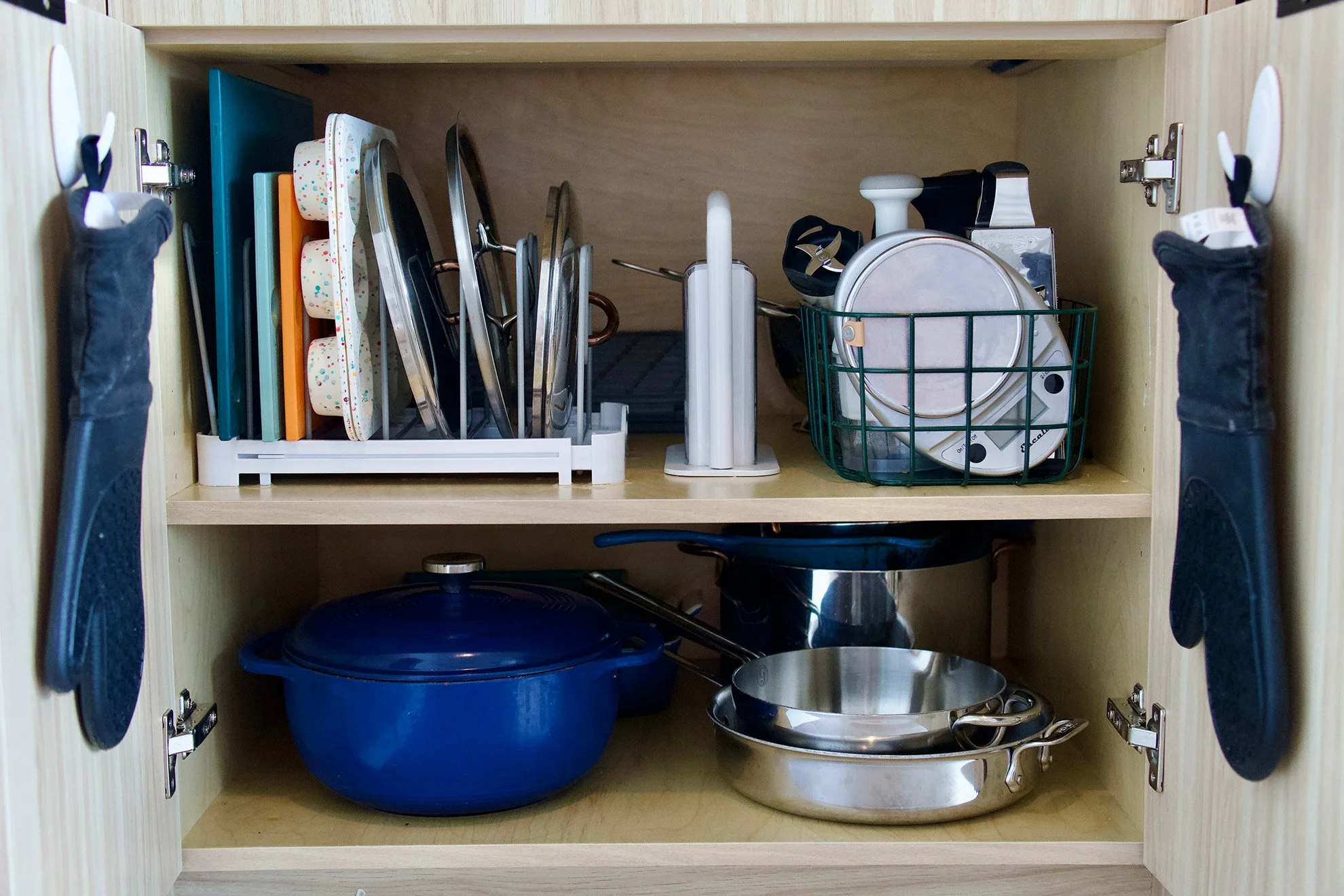 Open kitchen cabinet with cookware, plates, and utensils stored inside.