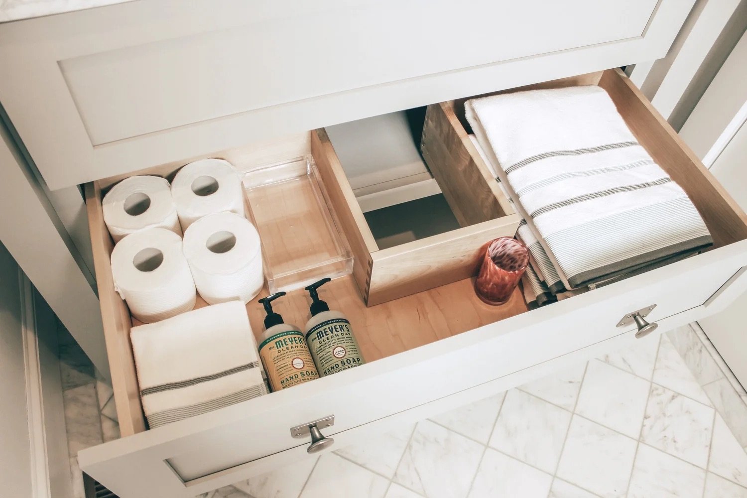 Organized bathroom drawer containing toilet paper rolls, hand soap bottles, folded towels, and a small container.