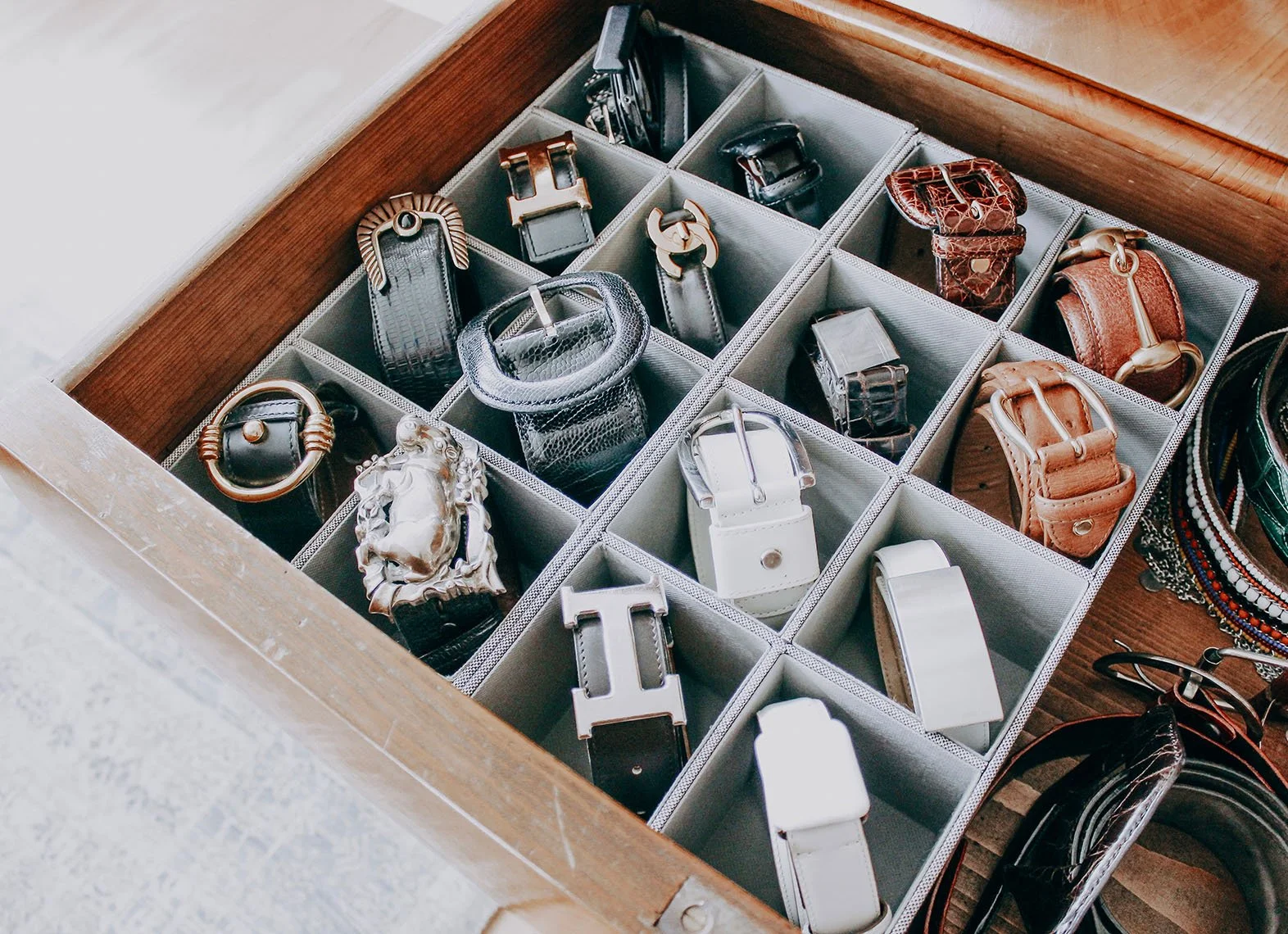 Open drawer containing various belts and accessories, arranged in a grid of compartments.