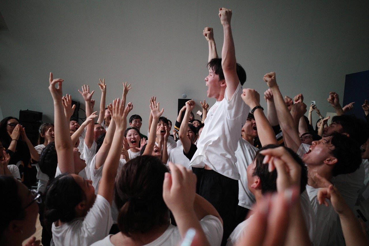 Group of young people celebrating, cheering, and raising their arms in a joyful crowd. This is from our Tour in Korea.
