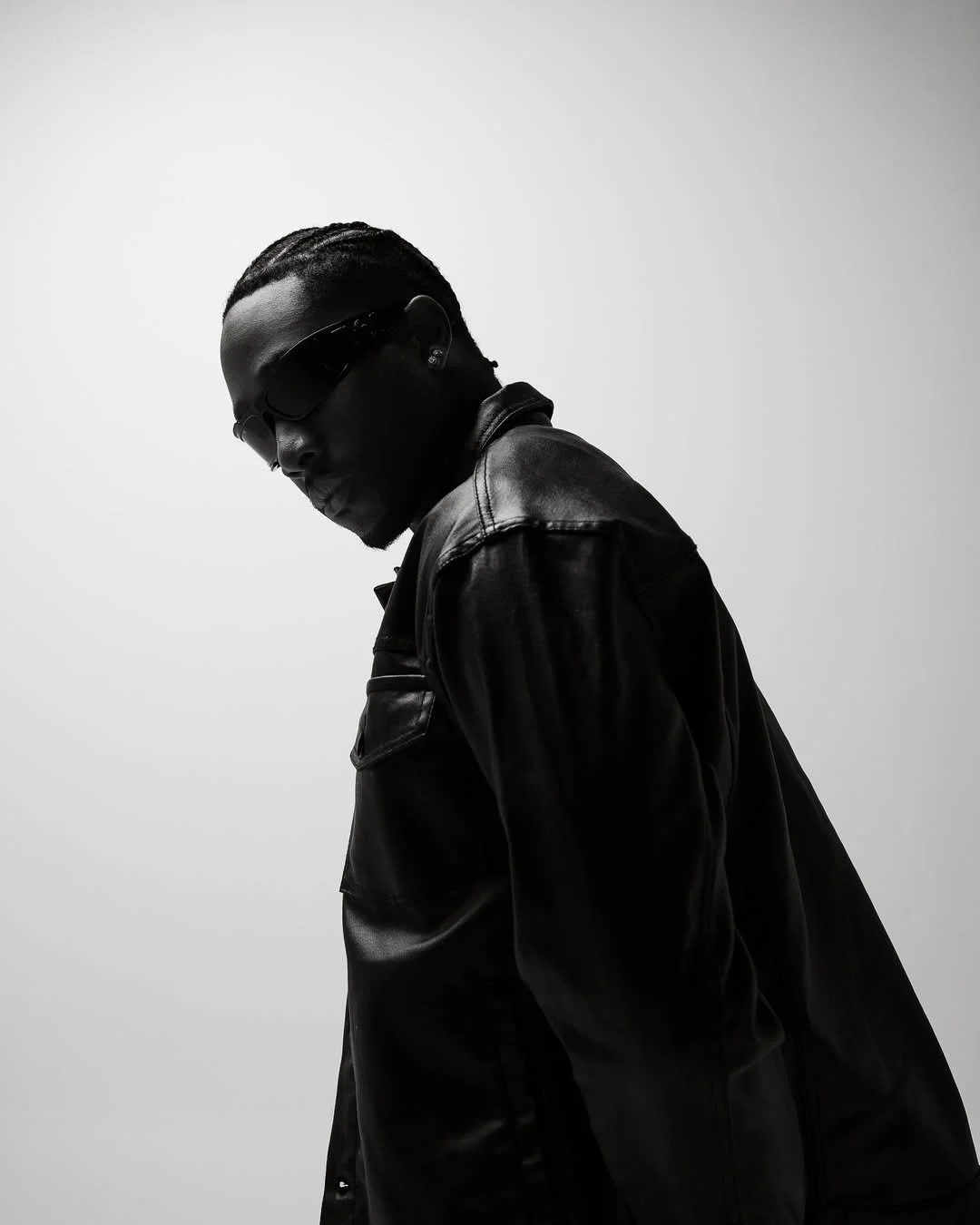 Black and white photo of a man wearing sunglasses and a leather jacket, looking down with a serious expression.