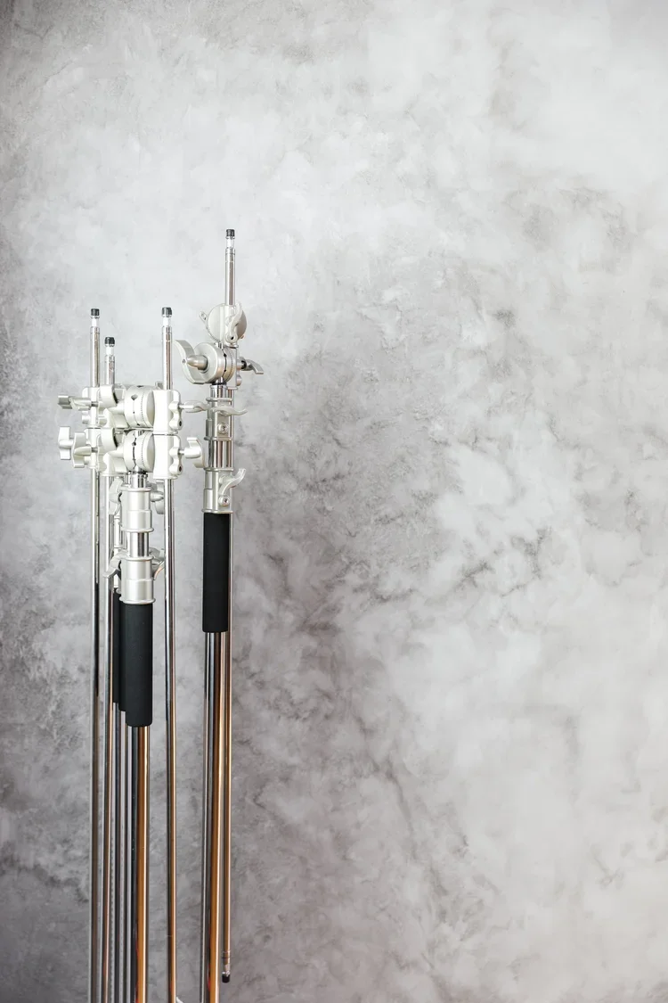 Three lean mic stands with adjustable boom arms and black foam grips leaning against a gray textured wall.