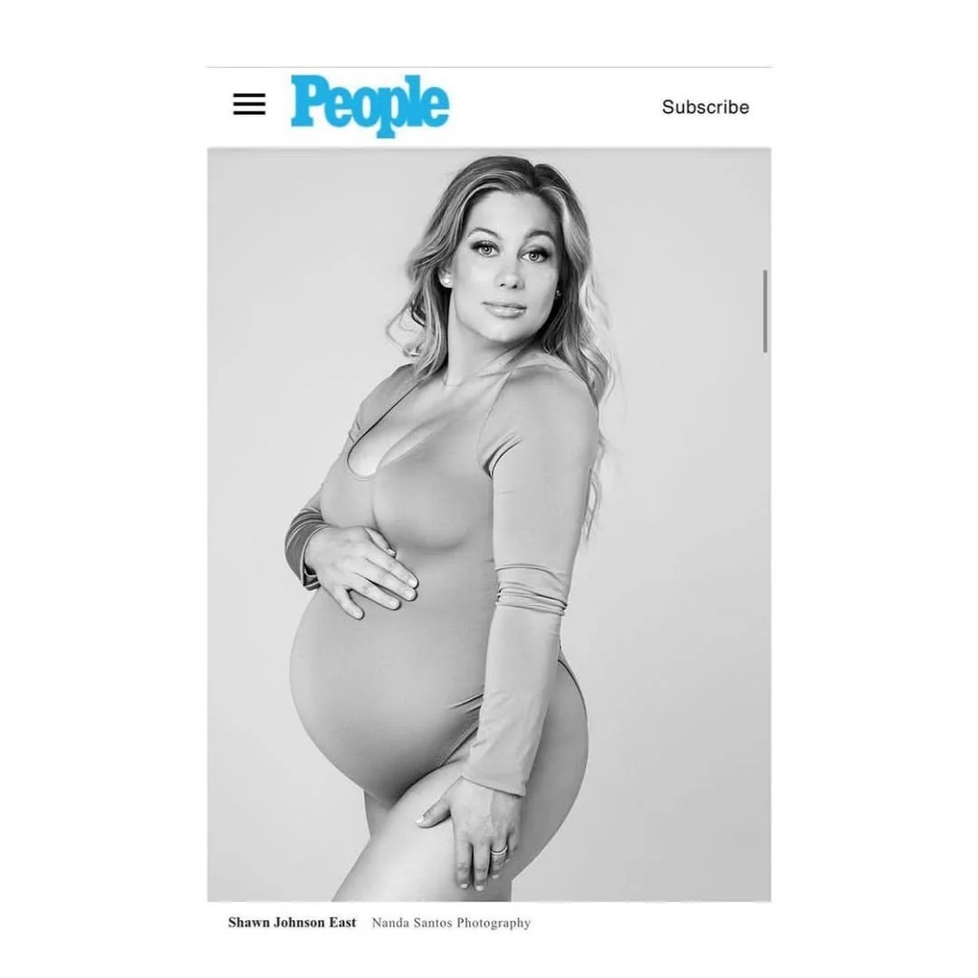 Black and white photo of a pregnant woman with long wavy hair, posing with her hand on her stomach, on the cover of People magazine.