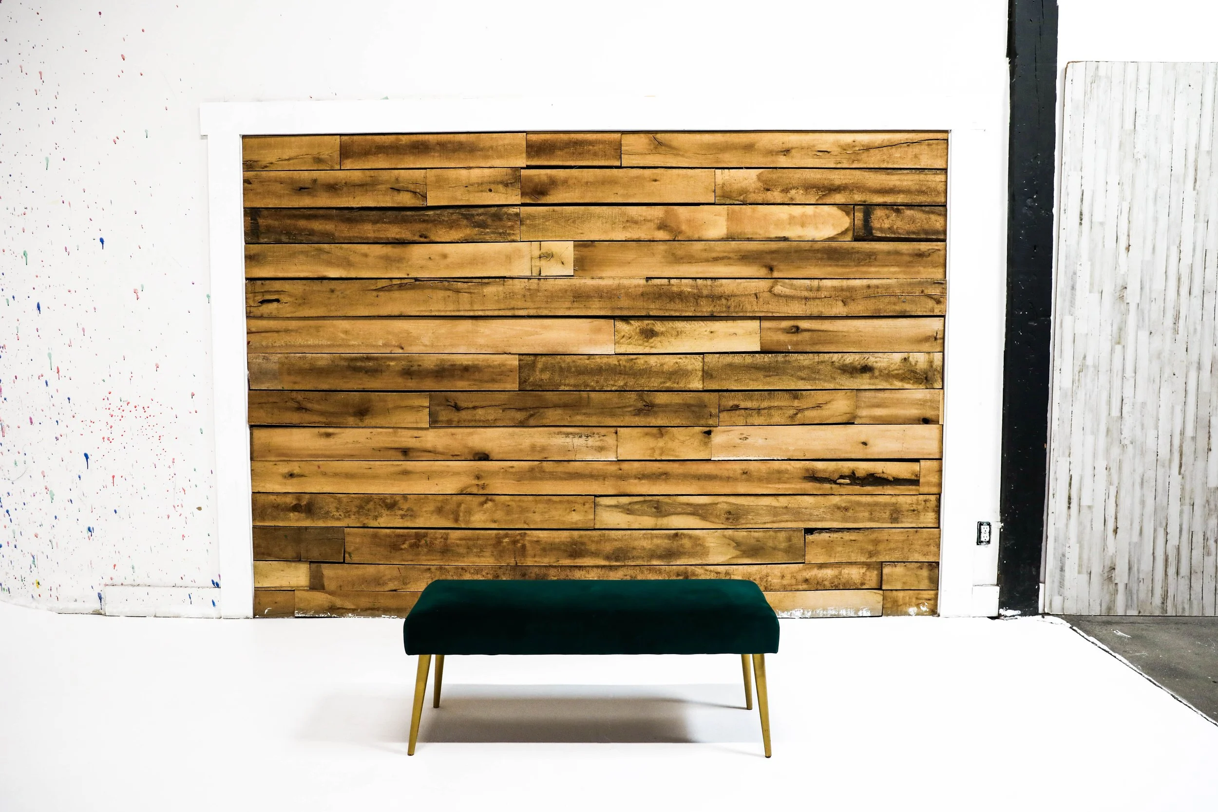 A green velvet bench with gold legs in front of a wooden wall with horizontal planks, in an industrial-style space.