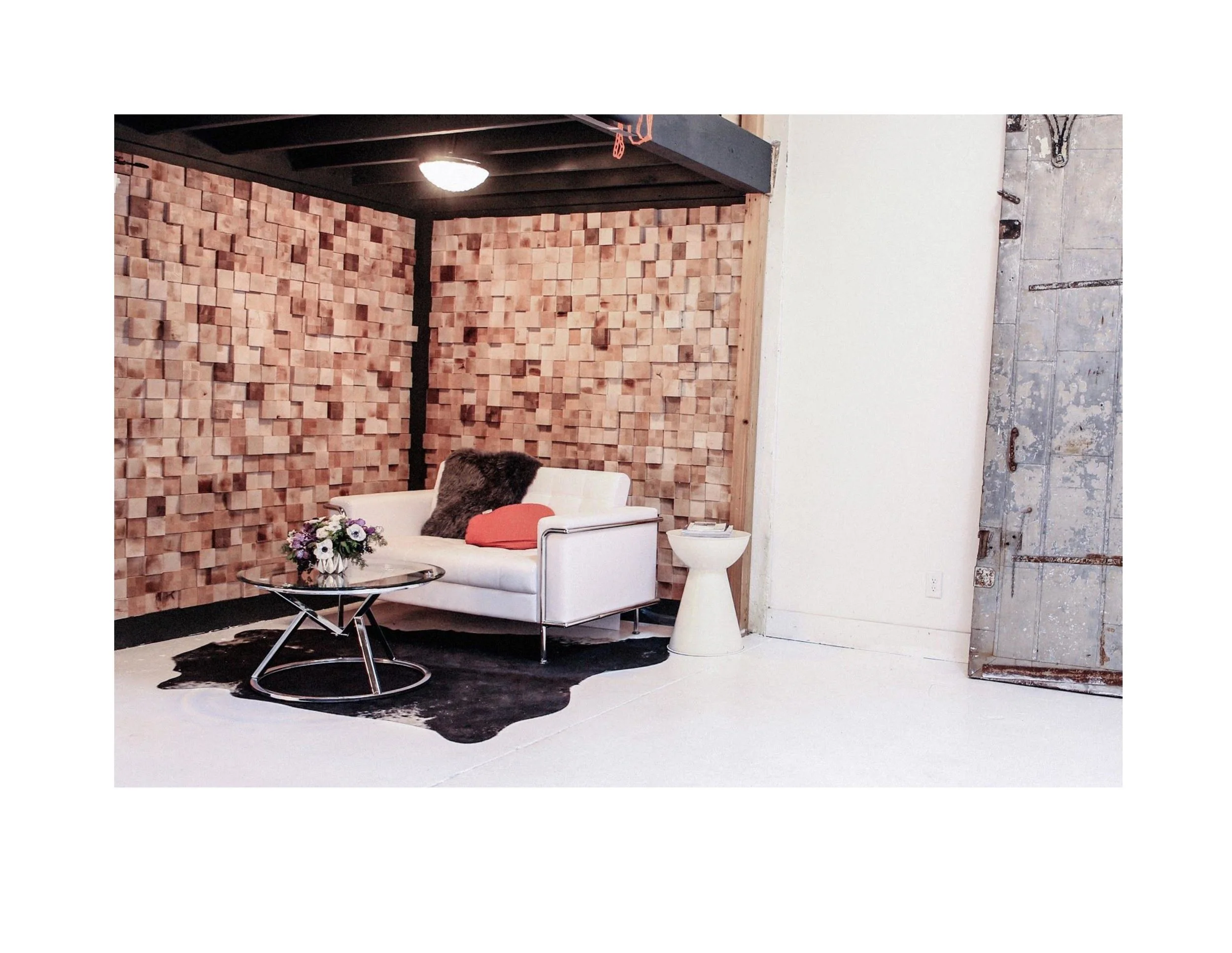 Interior of a modern studio with a textured wood accent wall, white sofa with decorative pillows, a glass coffee table with a flower arrangement, a small side table, and a vintage sliding barn door.