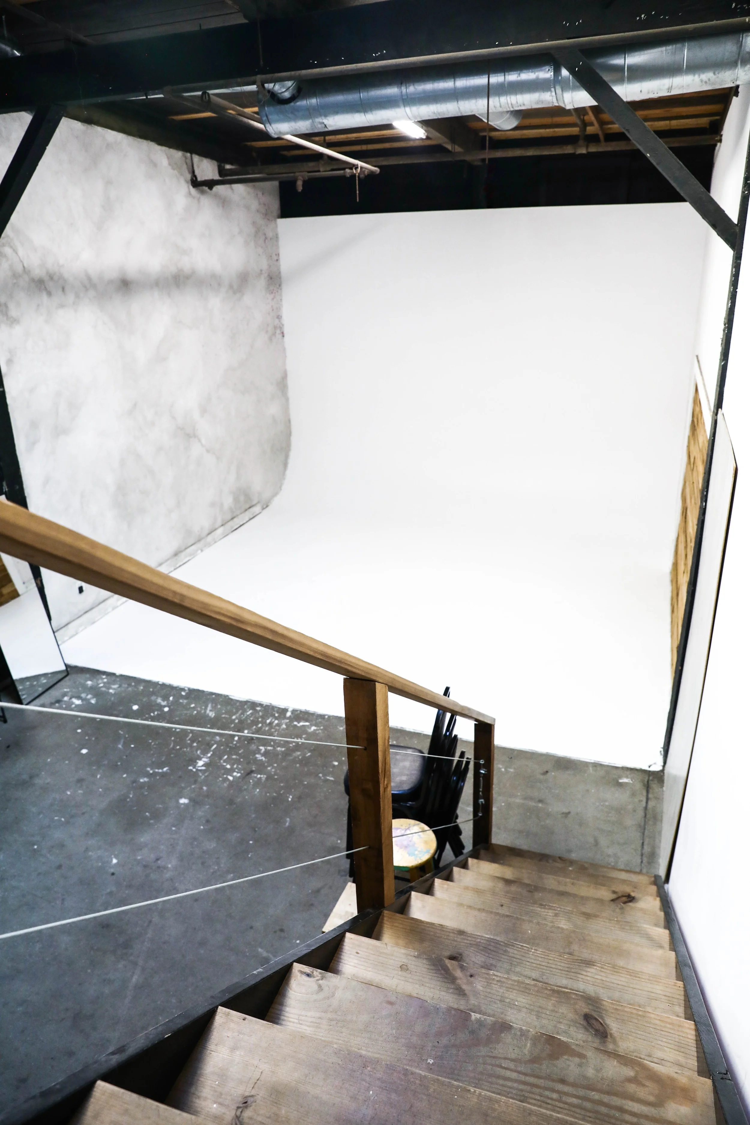 Empty photo studio with white infinity backdrop, wooden staircase, and black chairs.