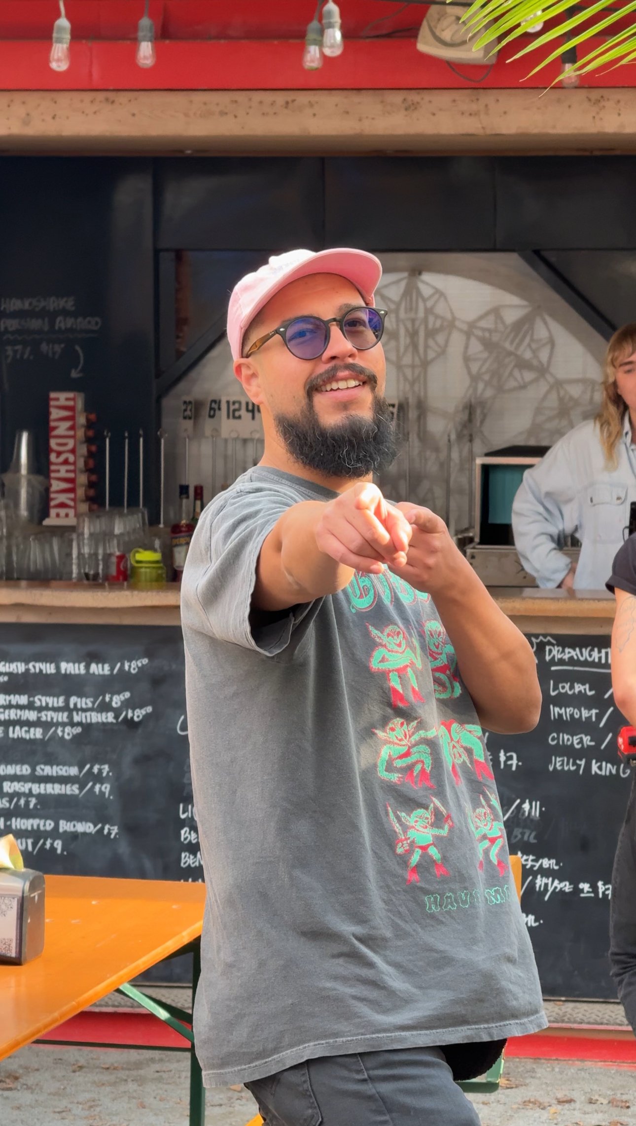 Neil is standing at a beer garden and pointing at the camera