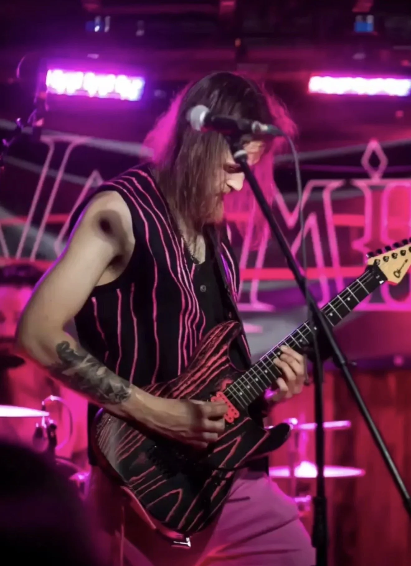 A musician playing an electric guitar on stage with pink neon lighting. He is wearing a custom painted vest by Neil Molloy.