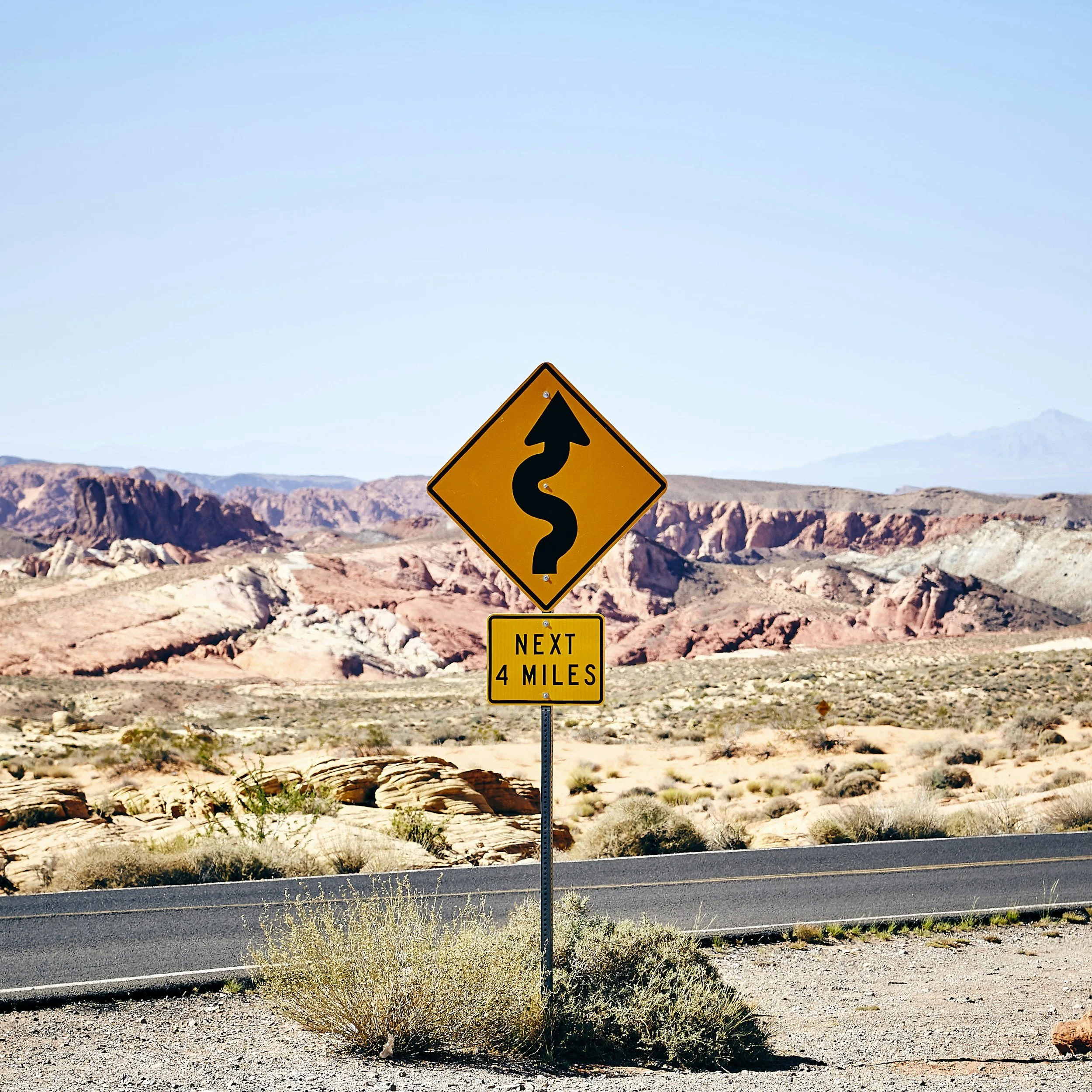 A road sign in a desert landscape indicating winding road for the next 4 miles.