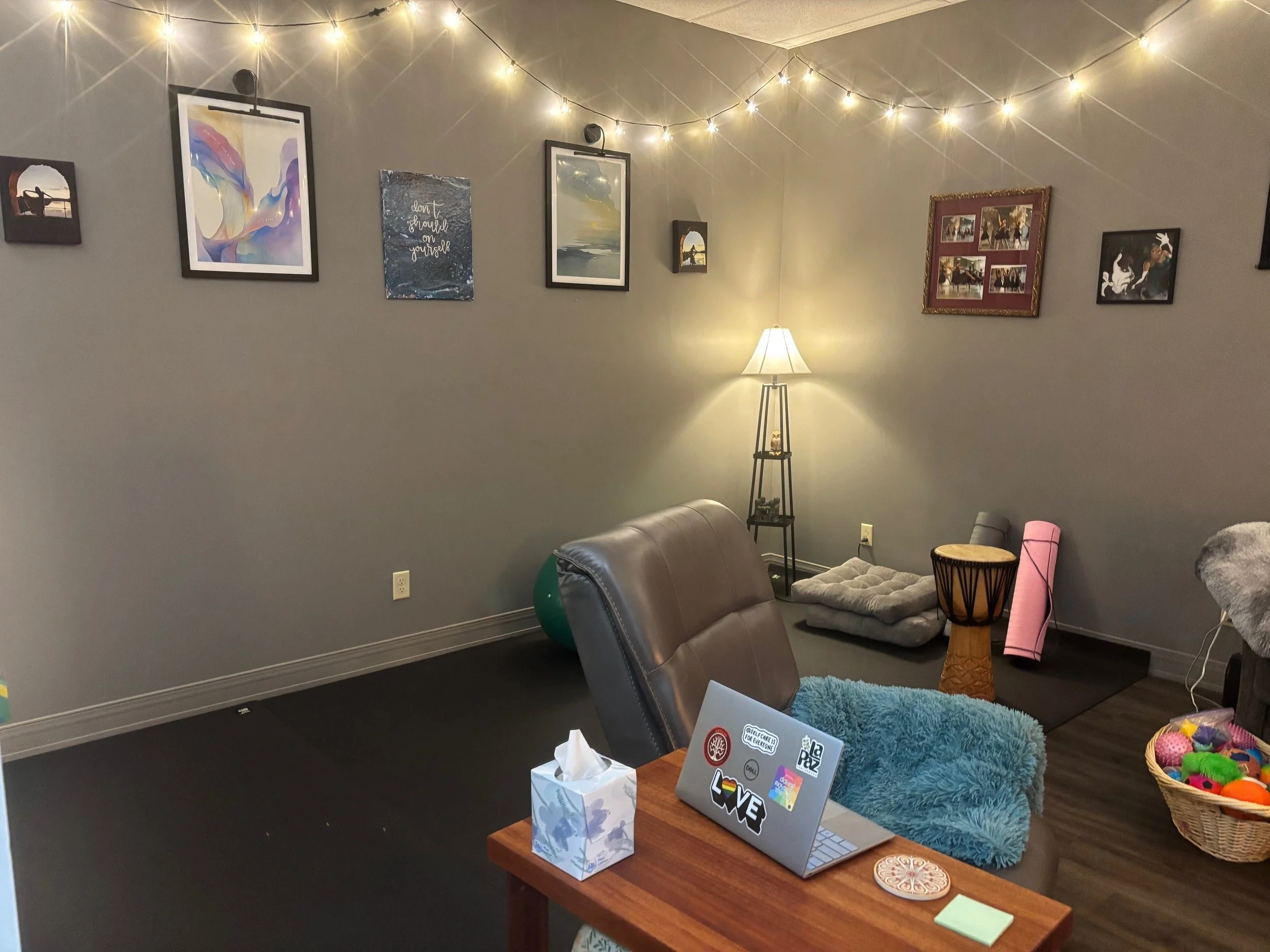 back half of the office showing computer table, chair, and mats, with light, yoga mats, a drum and meditation cushins