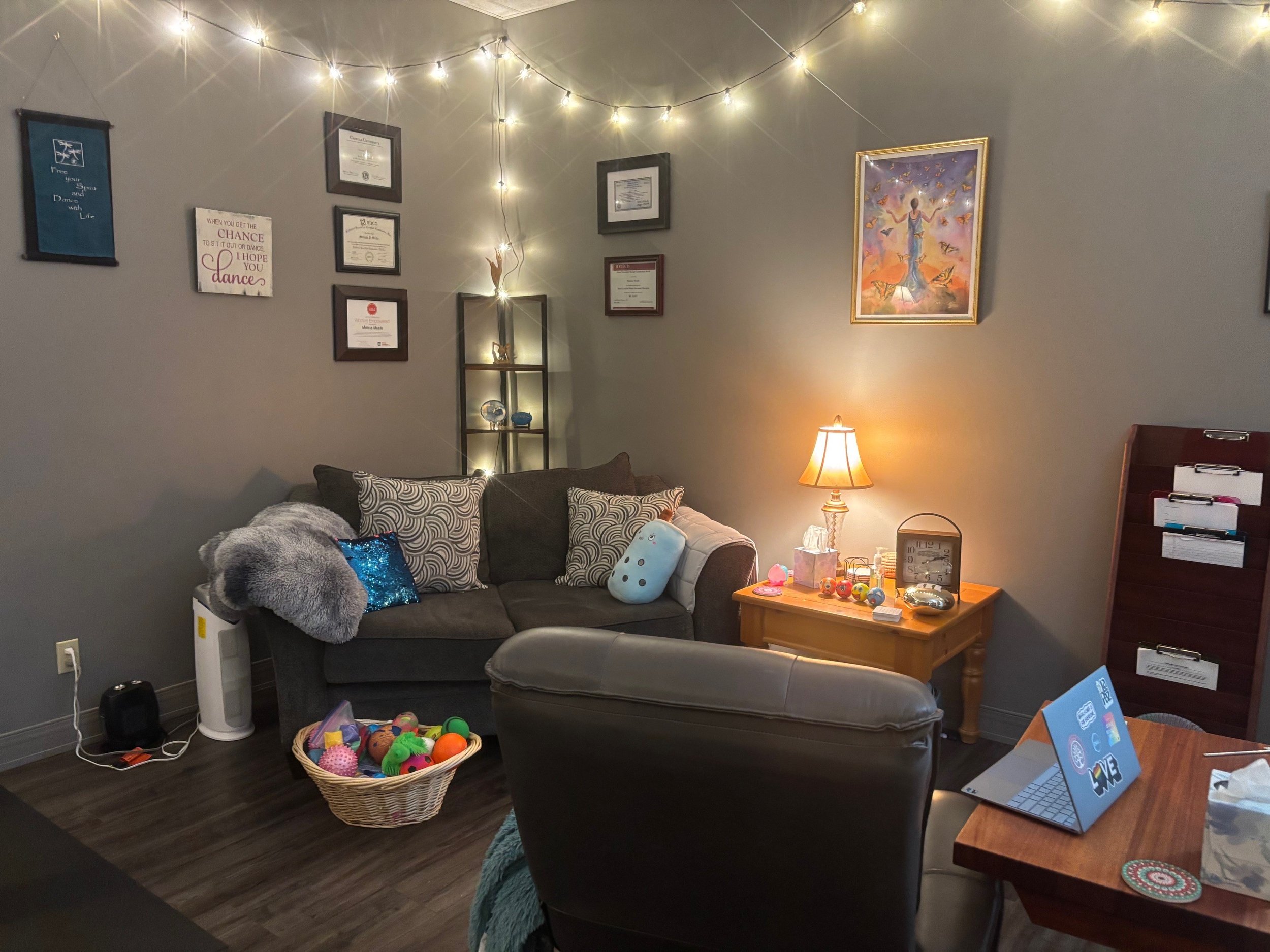 view of office showing couch, chair computer table, end table, file rack, and basket of fidgets