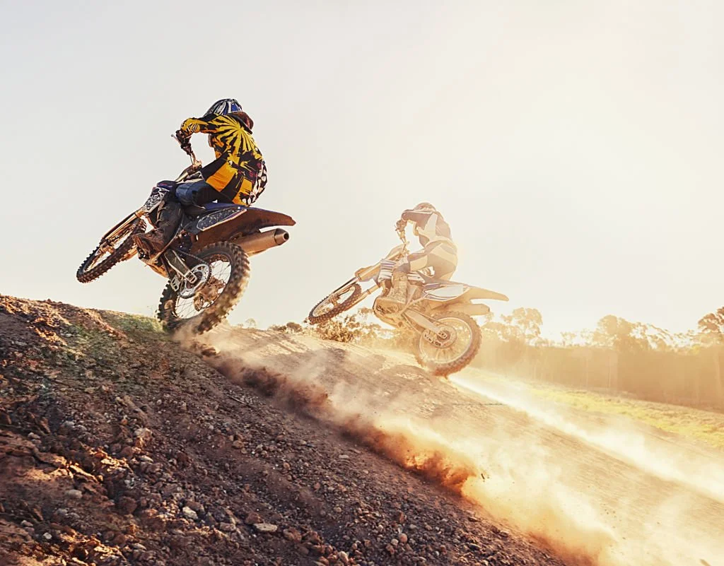 Two motocross riders jumping on dirt track with dust and sunlight in the background after filling up with VentPro