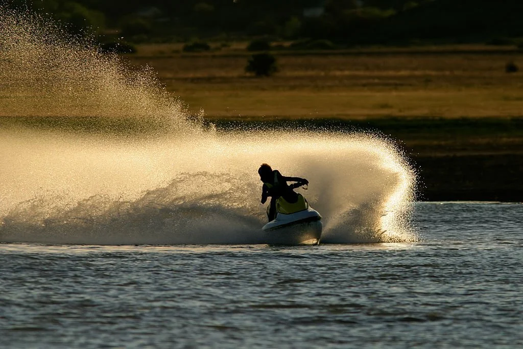 A person riding a jet ski on a body of water during sunset, creating a spray of water behind them after a fast fill-up with VentPro.