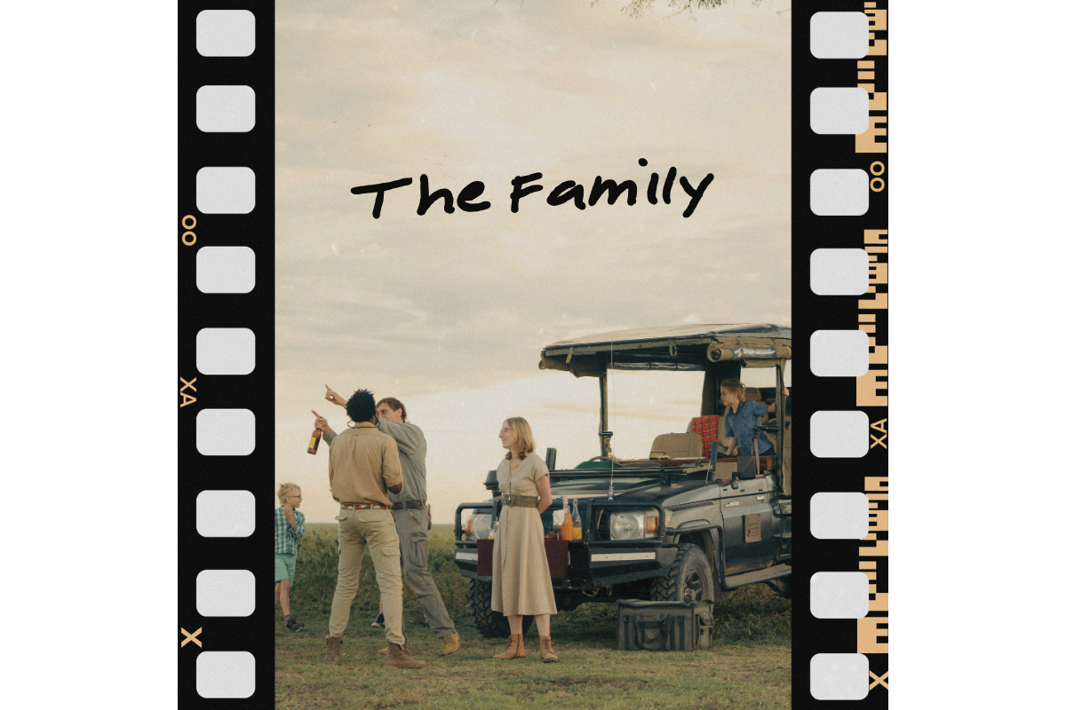 A family with children and two adults standing next to a safari-style vehicle outdoors under a cloudy sky, with the text "The Family" written above.