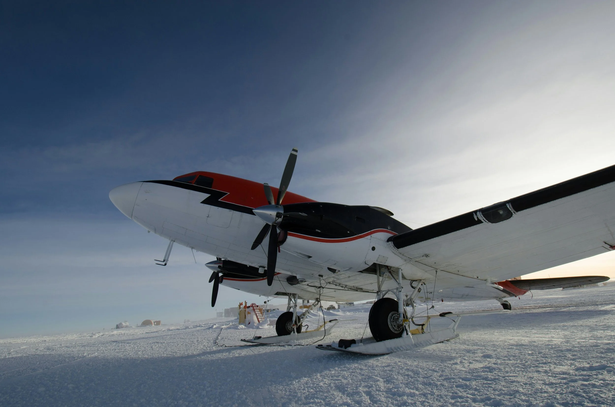 Small propeller airplane with skis on snow-covered ground under cloudy sky.