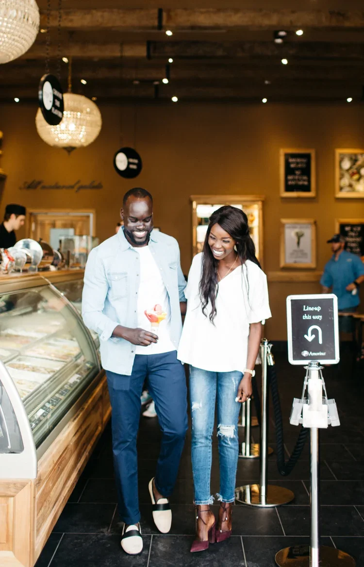 A smiling couple walking in an ice cream shop; the man holds an ice cream cone, and they seem happy and enjoying their outing.
