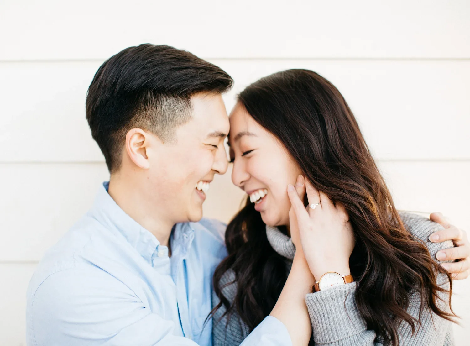 A smiling couple, a man and a woman, touch foreheads and hold each other affectionately indoors.
