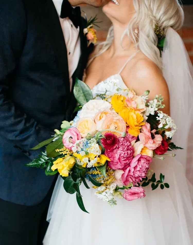 Bride and groom on their wedding day, holding a colorful bouquet of flowers.