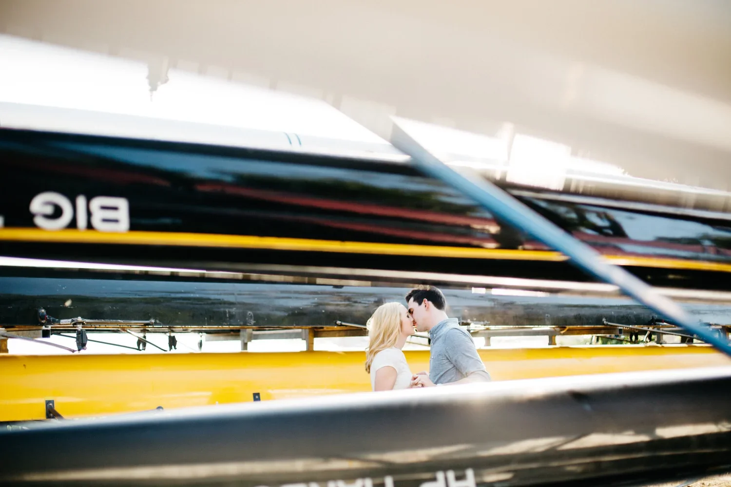 A couple sharing a kiss, framed by the tops of colorful rowing boats.