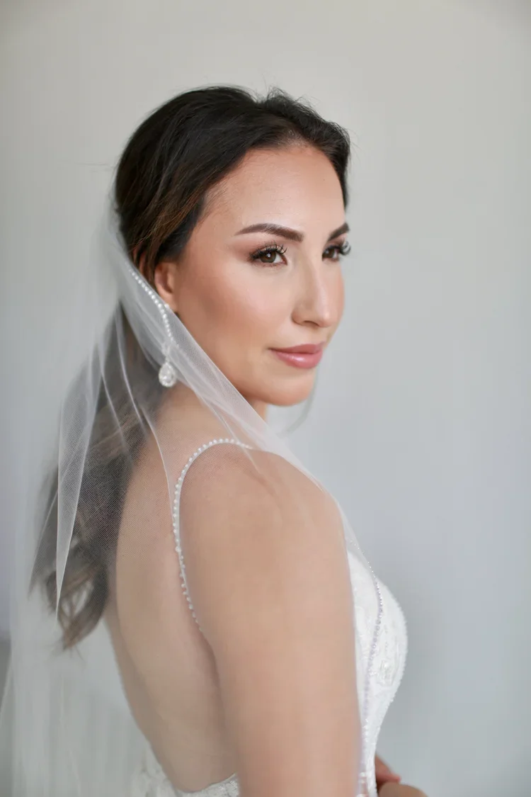 Beautiful woman on her wedding day wearing a white wedding gown and veil, with makeup and styled hair.