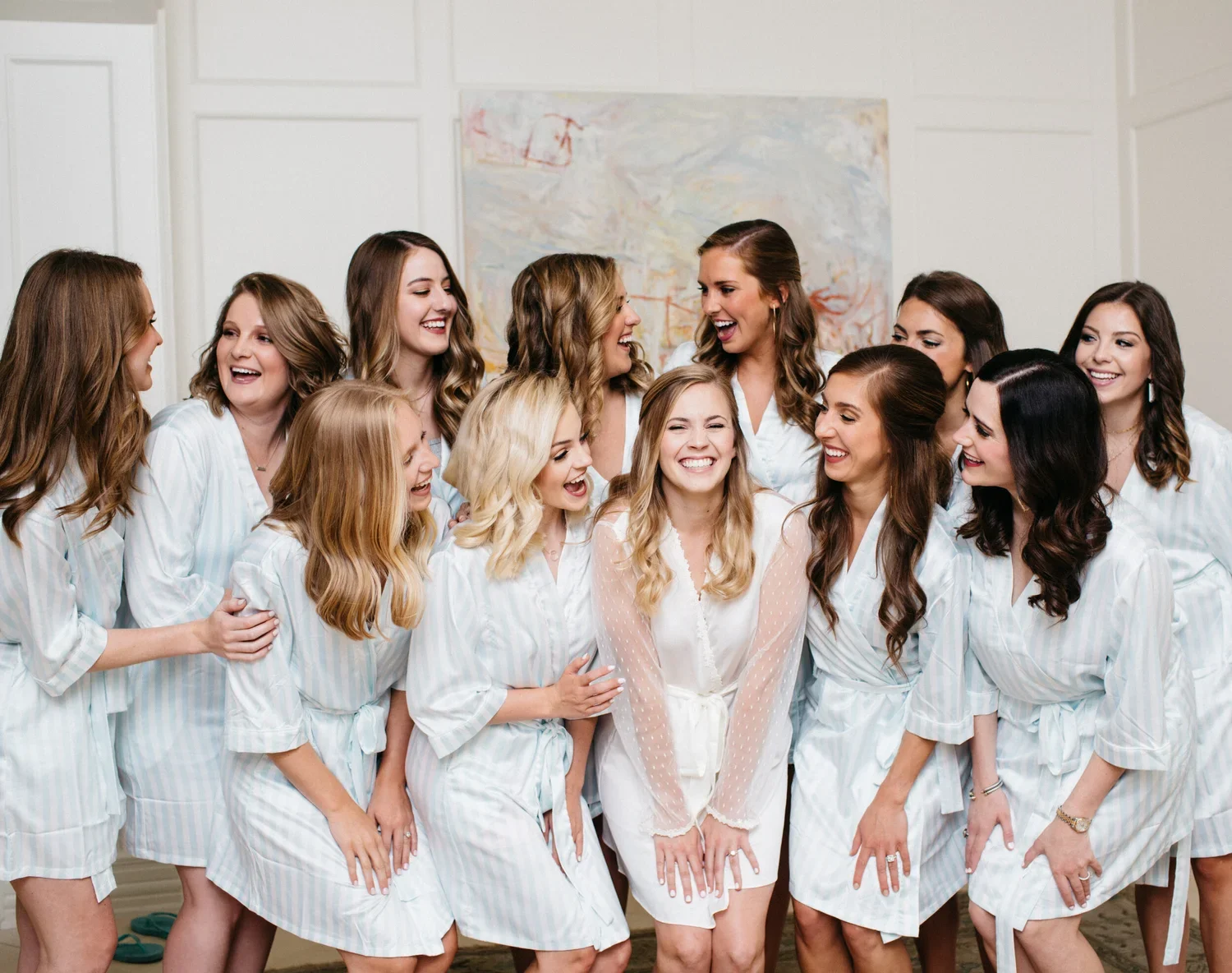 A group of women dressed in matching silky white pajamas, laughing and smiling together in a bright room.