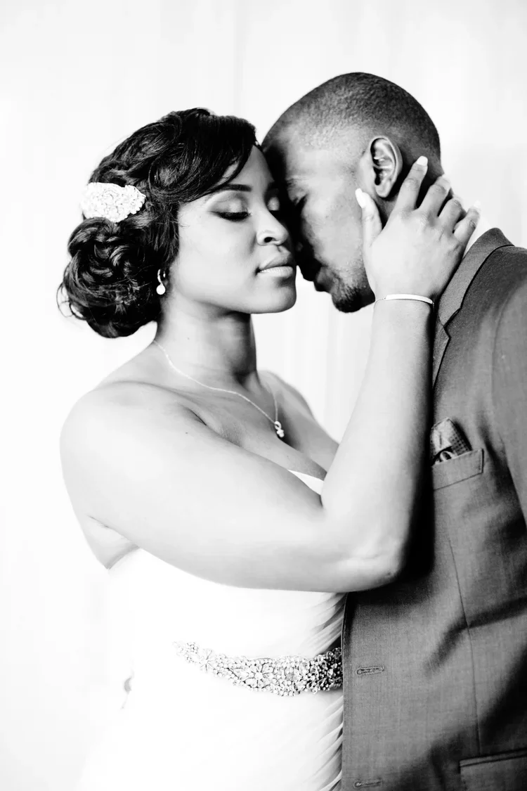 A black and white photo of a bride and groom in an intimate moment, with their foreheads touching and eyes closed.